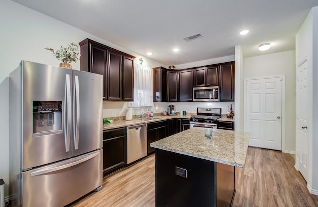 kitchen with light stone counters, dark brown cabinetry, stainless steel appliances, and a kitchen island