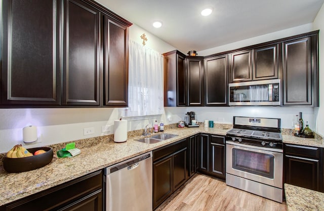 kitchen with sink, light stone counters, dark brown cabinets, appliances with stainless steel finishes, and light hardwood / wood-style floors