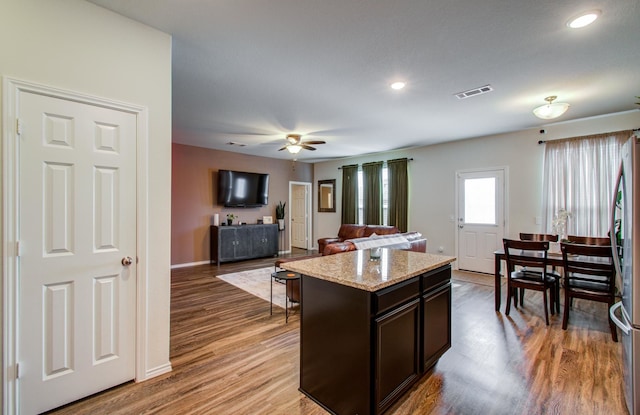 kitchen with a kitchen island, hardwood / wood-style flooring, ceiling fan, dark brown cabinetry, and light stone countertops