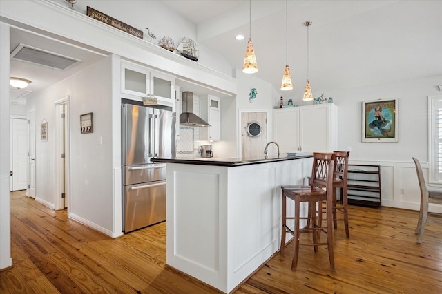 kitchen with high end fridge, white cabinetry, wall chimney exhaust hood, and light wood-type flooring