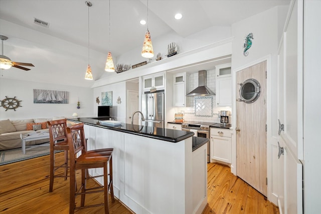 kitchen featuring a breakfast bar, wall chimney range hood, white cabinets, stainless steel appliances, and backsplash