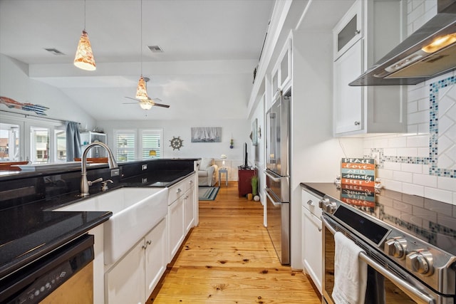 kitchen featuring appliances with stainless steel finishes, pendant lighting, sink, white cabinets, and wall chimney exhaust hood