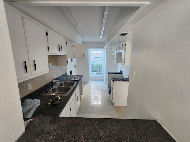 kitchen featuring sink, tasteful backsplash, light tile patterned floors, white cabinets, and stove