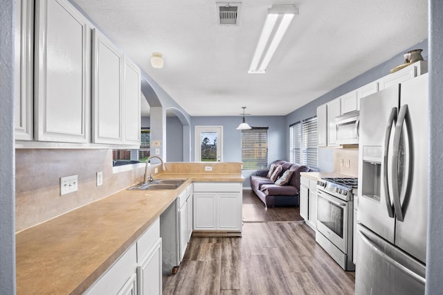 kitchen featuring pendant lighting, sink, stainless steel appliances, light hardwood / wood-style floors, and white cabinets