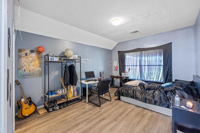 bedroom featuring lofted ceiling, light hardwood / wood-style flooring, and a textured ceiling