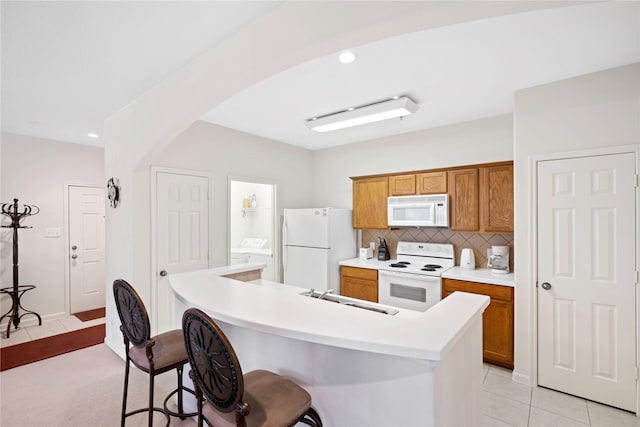 kitchen with sink, white appliances, a kitchen island with sink, backsplash, and a kitchen bar