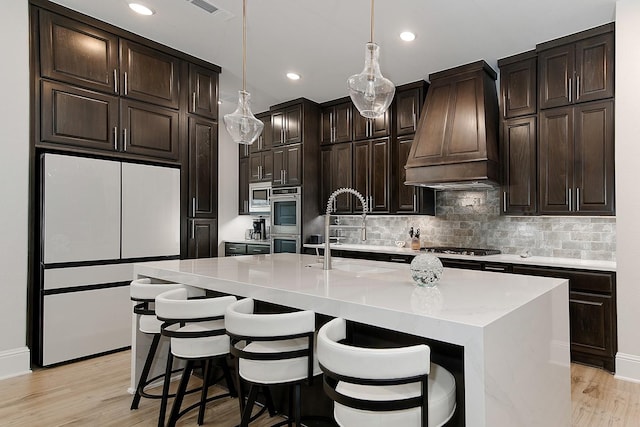 kitchen with premium range hood, appliances with stainless steel finishes, sink, a kitchen bar, and a kitchen island with sink