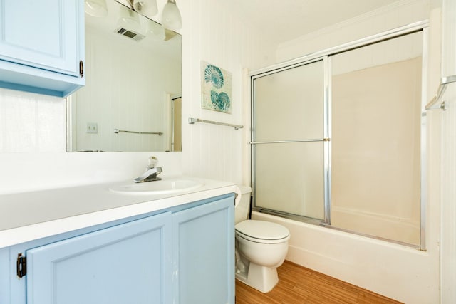 full bathroom with hardwood / wood-style floors, shower / bath combination with glass door, vanity, ornamental molding, and toilet