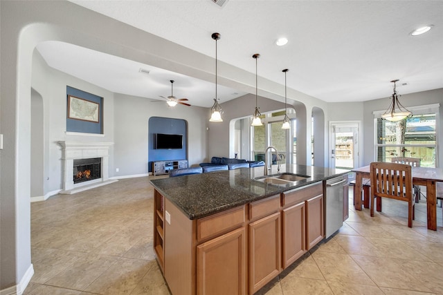 kitchen featuring sink, dishwasher, dark stone countertops, an island with sink, and decorative light fixtures