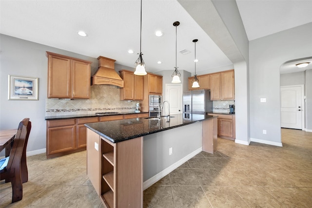 kitchen with sink, a kitchen island with sink, hanging light fixtures, stainless steel appliances, and custom exhaust hood