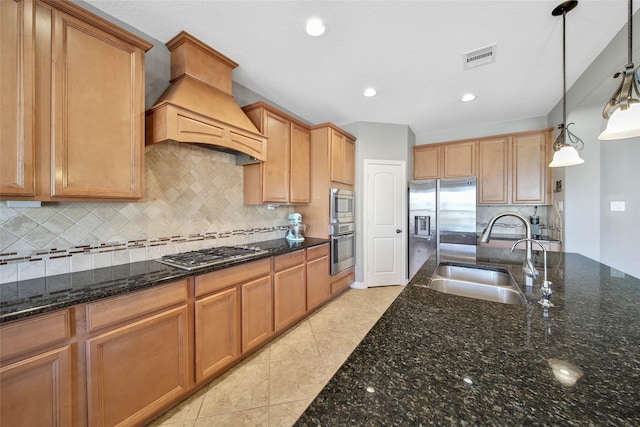 kitchen with appliances with stainless steel finishes, decorative light fixtures, sink, dark stone counters, and custom exhaust hood