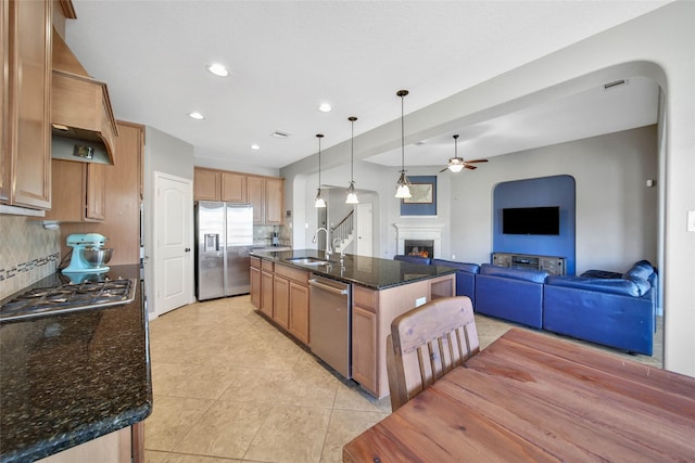 kitchen with tasteful backsplash, an island with sink, dark stone countertops, hanging light fixtures, and stainless steel appliances