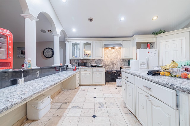 kitchen with extractor fan, white cabinetry, white fridge with ice dispenser, light stone countertops, and decorative columns