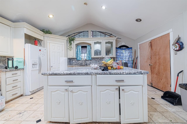 kitchen with vaulted ceiling, white cabinetry, backsplash, white refrigerator with ice dispenser, and light stone countertops