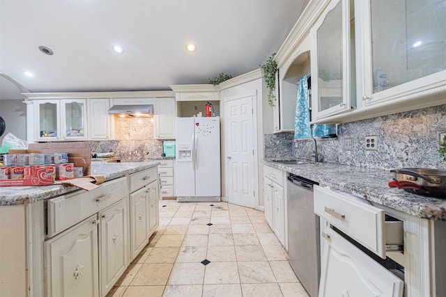 kitchen featuring dishwasher, sink, light stone countertops, and white fridge with ice dispenser