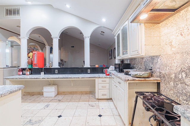 kitchen with light stone counters, white cabinetry, vaulted ceiling, and decorative columns