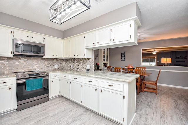 kitchen featuring light wood finished floors, tasteful backsplash, white cabinets, a peninsula, and stainless steel appliances