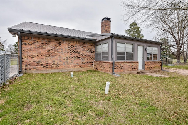 back of house with a chimney, metal roof, fence, a yard, and brick siding