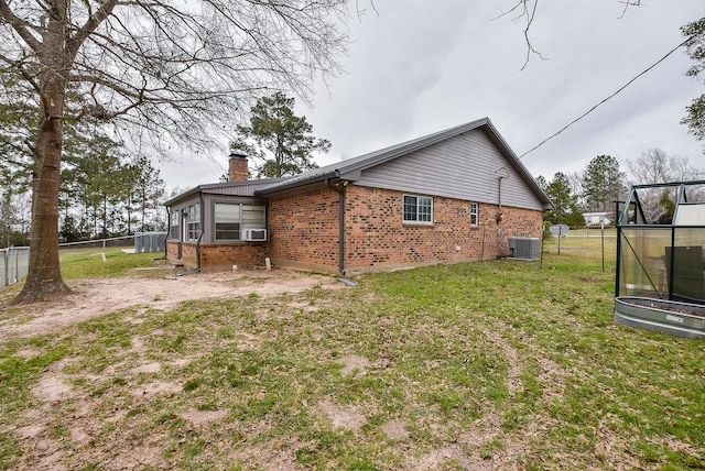 view of home's exterior featuring cooling unit, brick siding, fence, a yard, and a chimney