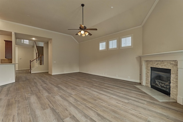 unfurnished living room with crown molding, ceiling fan, a stone fireplace, vaulted ceiling, and light wood-type flooring