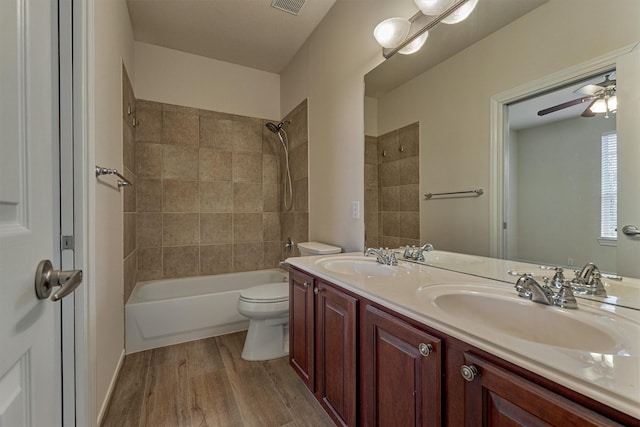 full bathroom featuring toilet, vanity, tiled shower / bath combo, hardwood / wood-style flooring, and ceiling fan