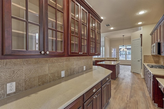 kitchen with pendant lighting, appliances with stainless steel finishes, backsplash, light hardwood / wood-style floors, and a textured ceiling