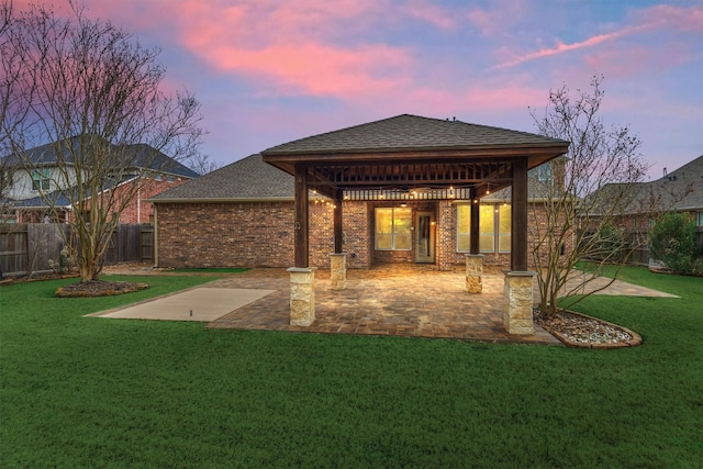 back house at dusk featuring a patio and a lawn