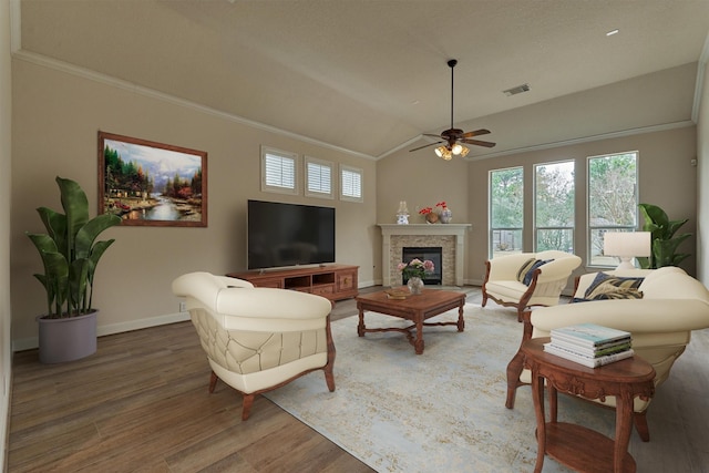 living room with lofted ceiling, a stone fireplace, wood-type flooring, and crown molding