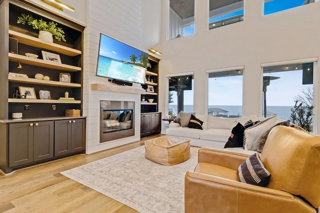 living room featuring a high ceiling, a healthy amount of sunlight, a large fireplace, and light hardwood / wood-style flooring