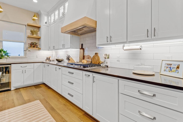 kitchen with white cabinetry, tasteful backsplash, light wood-type flooring, custom range hood, and beverage cooler