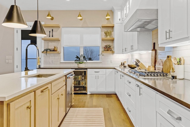 kitchen with premium range hood, appliances with stainless steel finishes, white cabinetry, sink, and hanging light fixtures