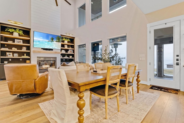 dining area featuring a towering ceiling, a fireplace, light hardwood / wood-style floors, and built in shelves