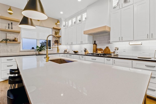 kitchen with custom exhaust hood, an island with sink, sink, and white cabinets