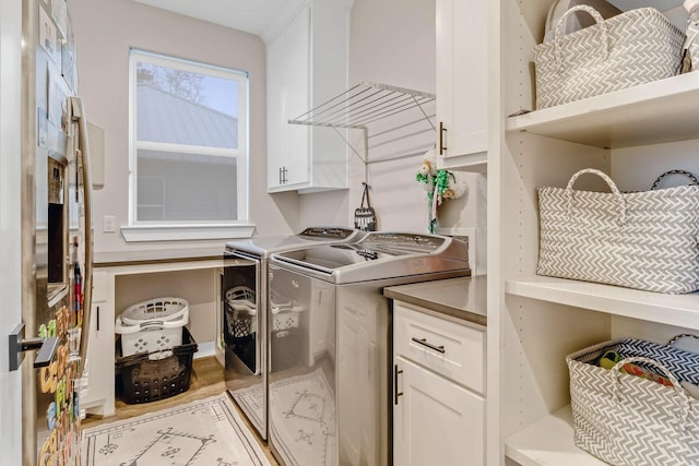 clothes washing area featuring cabinets, washing machine and clothes dryer, and light wood-type flooring