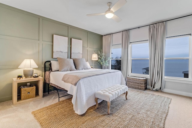 bedroom featuring light carpet, ceiling fan, and a water view