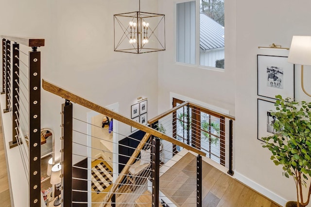 staircase with hardwood / wood-style flooring, a healthy amount of sunlight, an inviting chandelier, and a towering ceiling