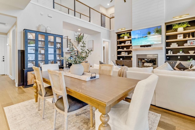 dining room with a high ceiling, a large fireplace, light hardwood / wood-style floors, and built in shelves