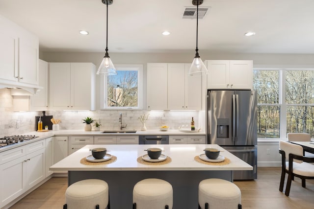 kitchen with pendant lighting, sink, white cabinetry, stainless steel appliances, and a center island