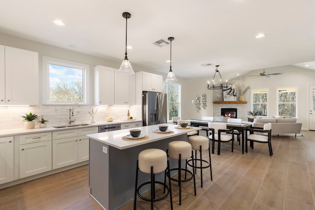 kitchen featuring sink, appliances with stainless steel finishes, white cabinetry, a kitchen island, and decorative light fixtures