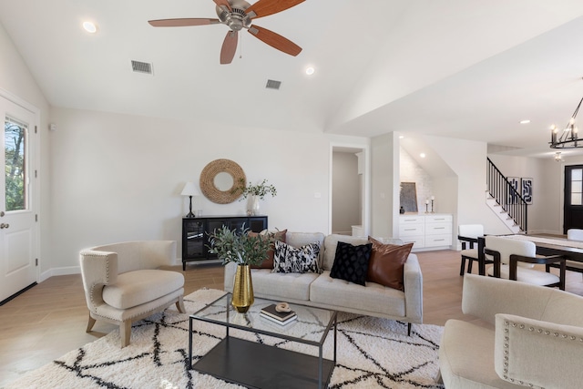 living room with vaulted ceiling, ceiling fan with notable chandelier, and light wood-type flooring