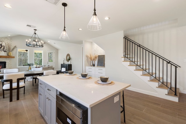 kitchen with a stone fireplace, a center island, stainless steel microwave, and decorative light fixtures