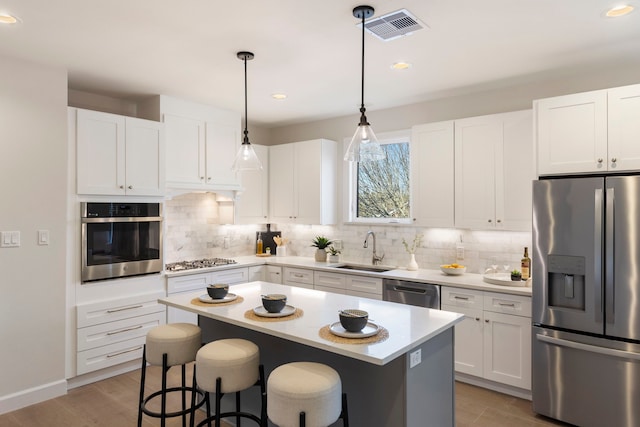 kitchen featuring sink, white cabinetry, a center island, hanging light fixtures, and stainless steel appliances