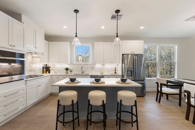 kitchen with stainless steel appliances, a breakfast bar, white cabinets, and decorative light fixtures