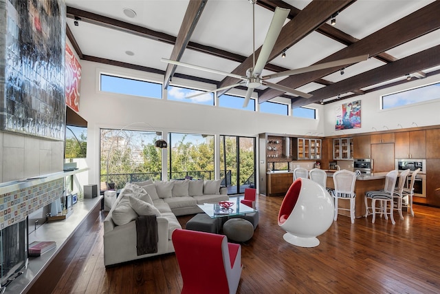 living room with ceiling fan, dark hardwood / wood-style flooring, beam ceiling, and a towering ceiling