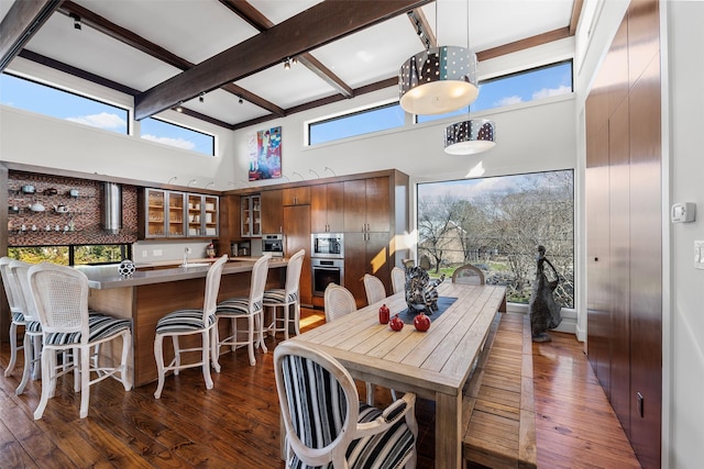 dining space with dark hardwood / wood-style floors, sink, beam ceiling, and a towering ceiling