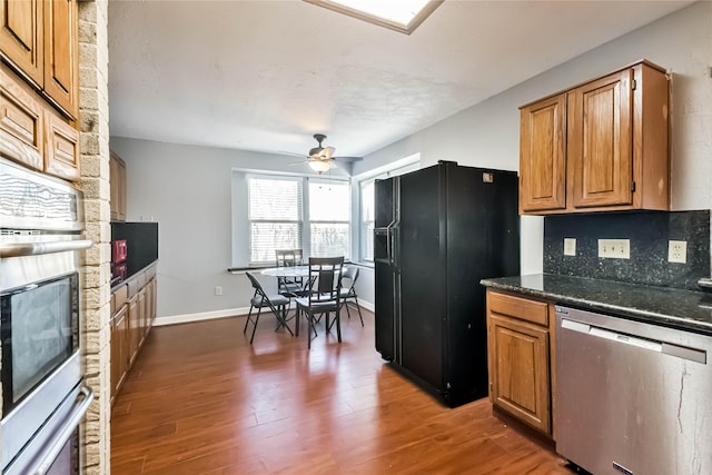 kitchen featuring dark wood-type flooring, a stone fireplace, dark stone countertops, appliances with stainless steel finishes, and decorative backsplash