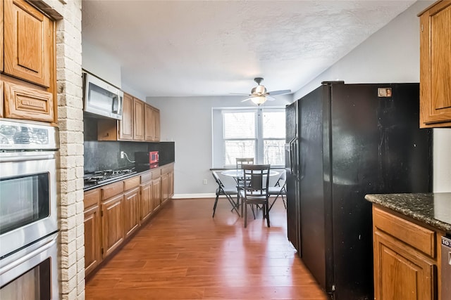 kitchen with dark stone countertops, dark hardwood / wood-style flooring, decorative backsplash, black appliances, and a textured ceiling