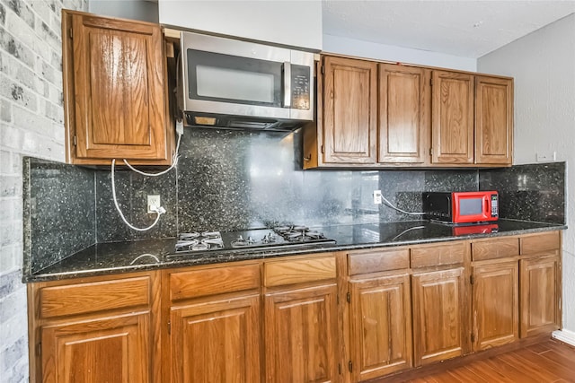 kitchen featuring tasteful backsplash, black gas stovetop, light hardwood / wood-style flooring, and dark stone countertops