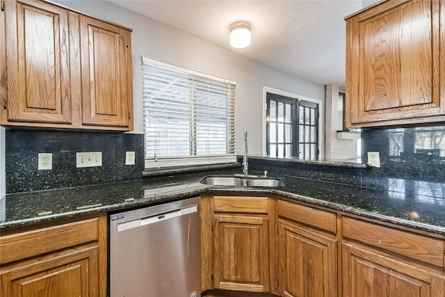 kitchen featuring stainless steel dishwasher, dark stone counters, sink, and backsplash