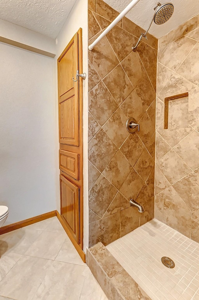 bathroom with tile patterned flooring, tiled shower, a textured ceiling, and toilet